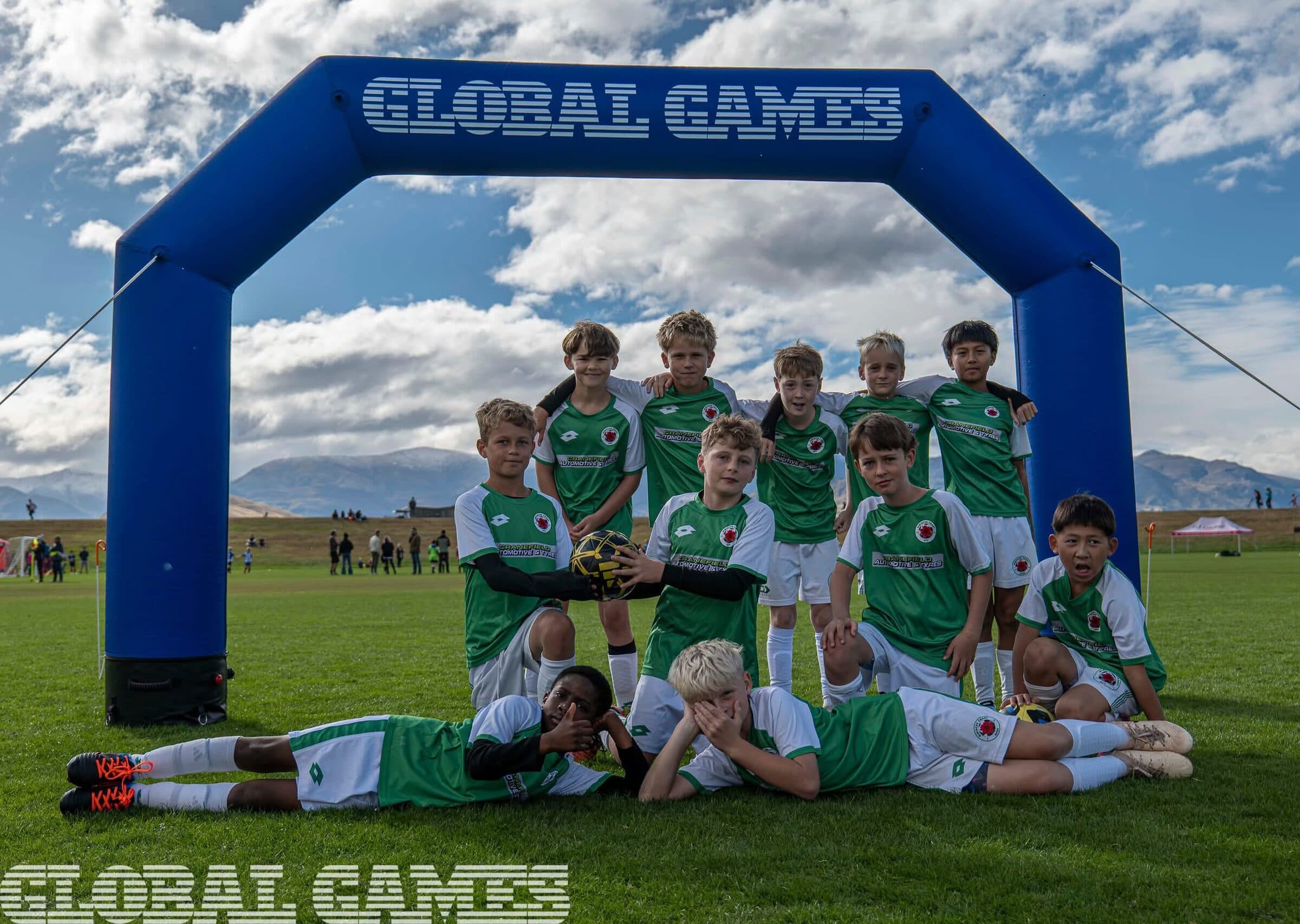 A team in green and white posing together under the inflatable Global Games arch